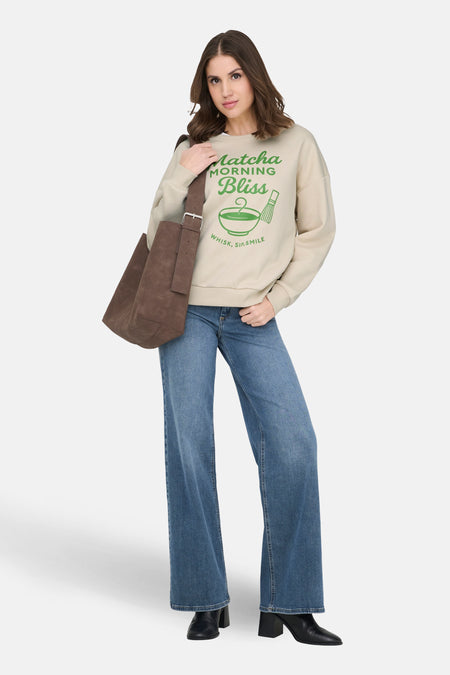 Ecru sweater van ONLY met groene print, gedragen met blauwe jeans en zwarte laarzen.