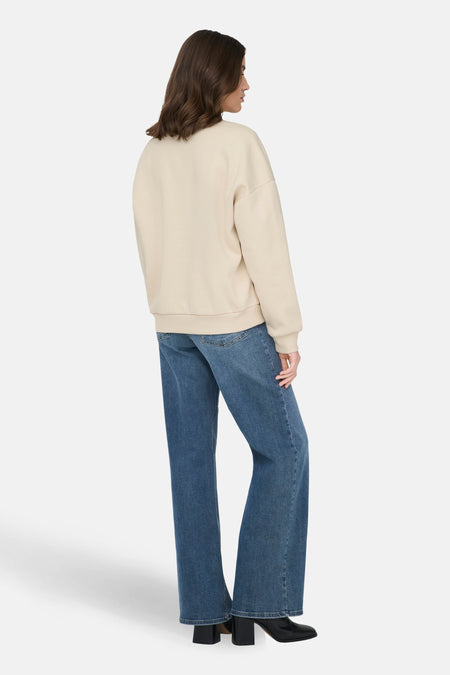 Ecru sweater van ONLY, met lange mouwen, gecombineerd met blauwe jeans en zwarte laarzen met hak.