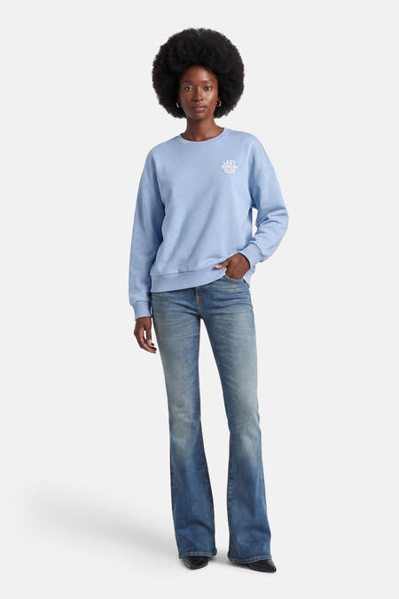 Blauwe sweater van ONLY, met een ronde hals en "Lazy Sunday Club"-opdruk op de borst, gedragen met jeans.
