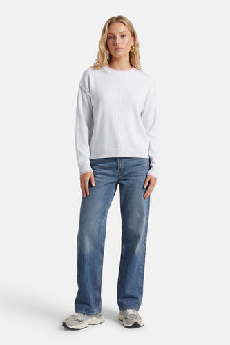 Pull blanc à col rond de JDY, avec des accents roses sur les bords et porté avec un jean bleu et des baskets grises.