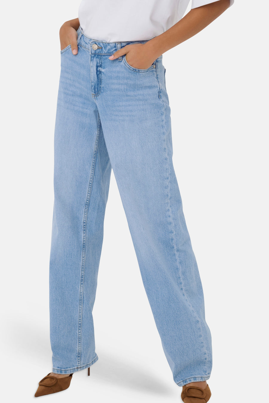 Rechte jeans van lichtblauw denim van JDY, gedragen door een model met handen in de zakken, met een wit T-shirt en bruine suède hakken.