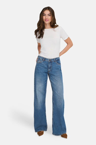 Mid-blauwe denim wide leg jeans van JDY, gedragen met een wit T-shirt en bruine schoenen.