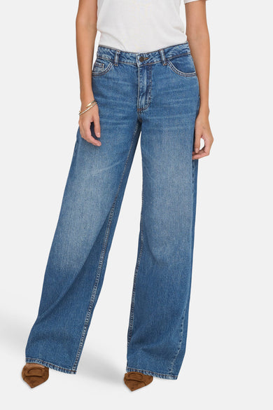 Jean large bleu moyen de JDY avec bouton métallique, délavage clair et un haut blanc.