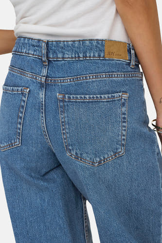 Jean large en denim bleu moyen de JDY, vue de dos, avec patch en cuir marron, coutures orange et poches arrière, porté avec un t-shirt blanc.