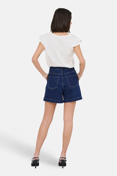 Donkerblauwe denim short van JDY, gezien van achteren met witte top en zwarte hakken.
