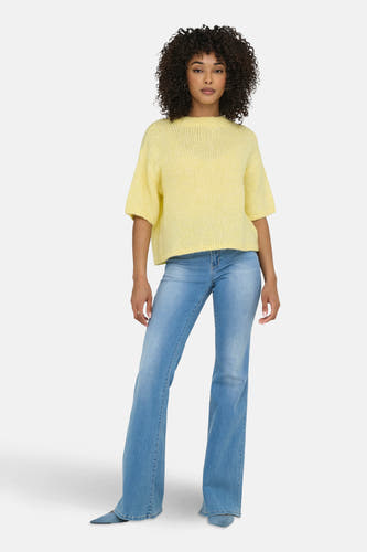 Gele trui met ronde hals van JDY, gecombineerd met een blauwe jeans met uitlopende pijpen en blauwe hakken.
