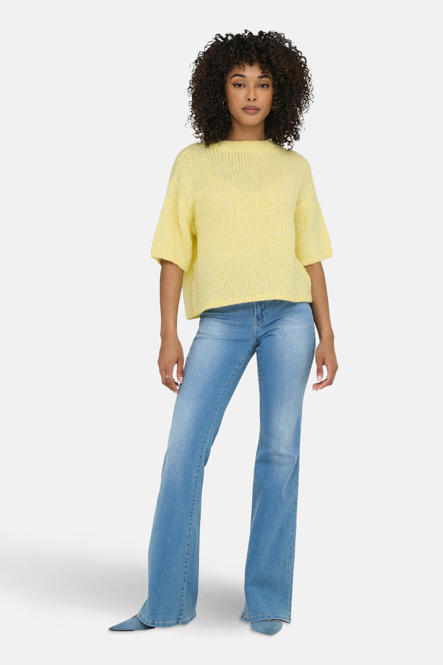 Gele trui met ronde hals van JDY, gecombineerd met een blauwe jeans met uitlopende pijpen en blauwe hakken.
