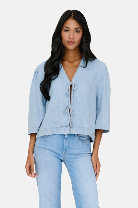 Chemisier en denim bleu clair de ONLY avec manches trois-quarts et fermeture boutonnée, porté avec un jean et des bottes en daim.