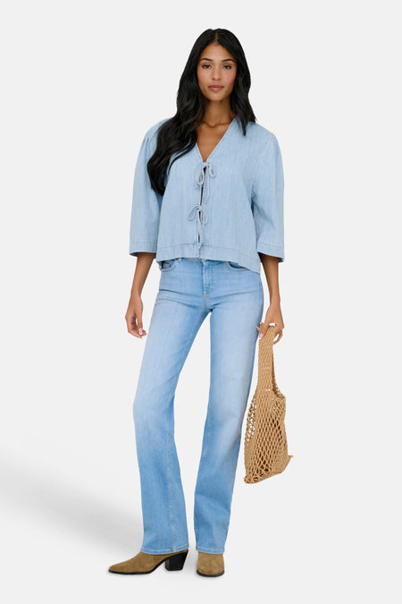Lichtblauwe denim blouse van ONLY met driekwart mouwen en een knoopsluiting, gedragen met een jeans en suède laarzen.
