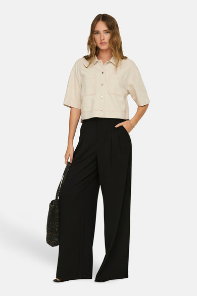 Chemise écru ONLY®, à manches courtes, fermeture boutonnée et poches plaquées, combinée avec un pantalon noir ample et un sac.