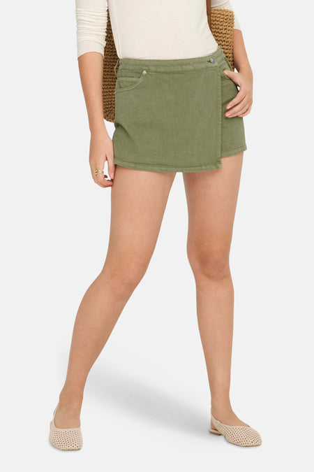 Skort kaki de ONLY, avec un design portefeuille et porté avec un haut blanc et un sac tressé.