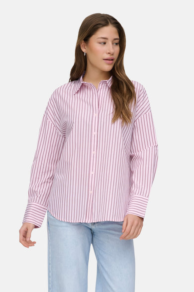 Chemise rose à manches longues ONLY, rayée, associée à un jean ample et des chaussures bleues.