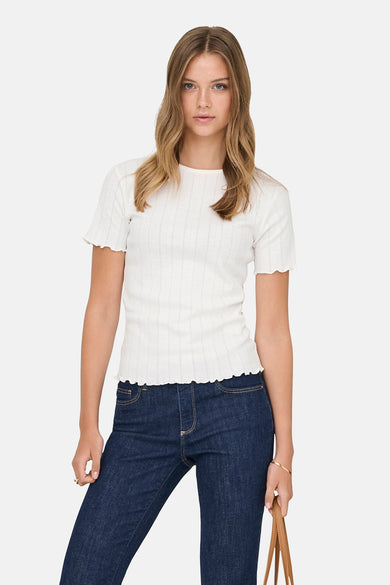 T-shirt blanc à manches courtes ONLY, avec une texture côtelée et un bord ondulé, associé à un jean foncé et des talons marron.