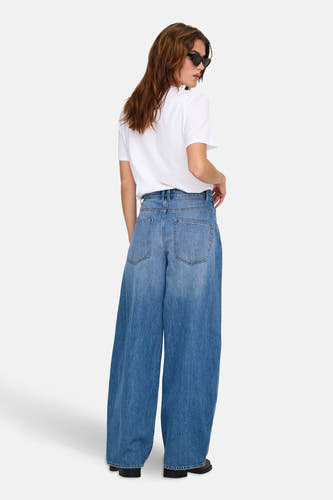 Jean spécial fit en denim bleu clair de ONLY, avec des jambes larges et un look usé, associé à un T-shirt blanc et à un chapeau de soleil.