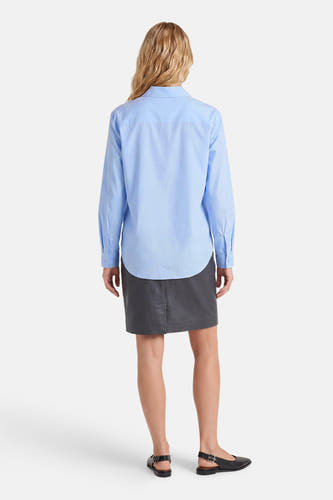 Blauw hemd met lange mouwen van JDY, van achteren gezien, met een gebogen zoom, gedragen met een donkergrijze rok en zwarte slingback ballerina's.