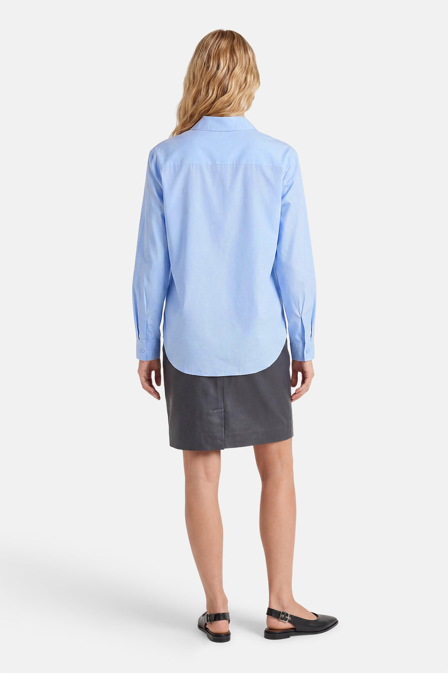 Blauw hemd met lange mouwen van JDY, van achteren gezien, met een gebogen zoom, gedragen met een donkergrijze rok en zwarte slingback ballerina's.