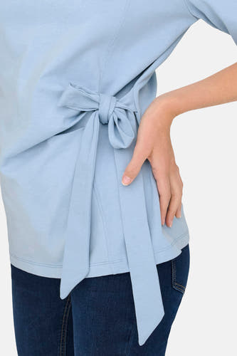 T-shirt bleu à manches courtes de ONLY, avec un détail de nœud sur le côté et porté avec un jean foncé.