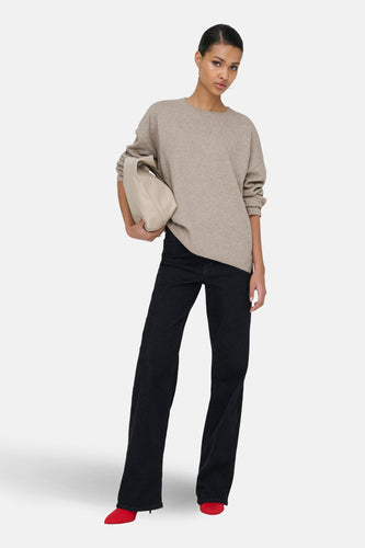 Model in beige sweater, zwarte jeans en rode schoenen.