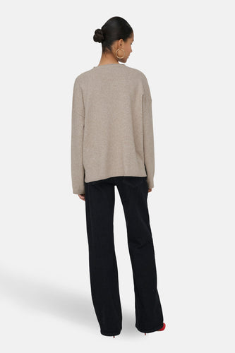 Vrouw met beige trui en zwarte jeans, gezien van achteren.