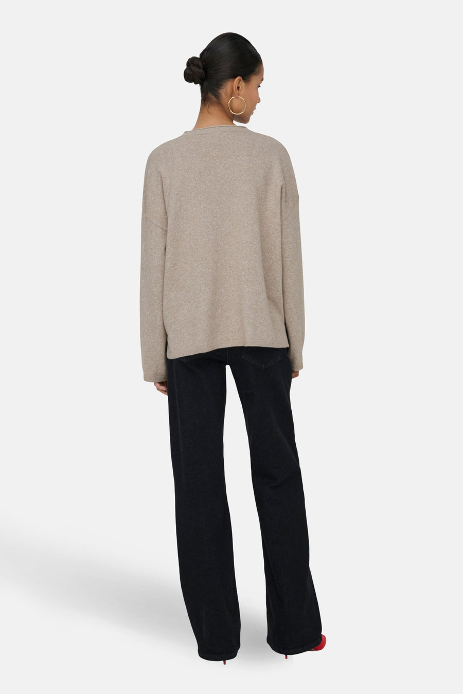 Vrouw met beige trui en zwarte jeans, gezien van achteren.