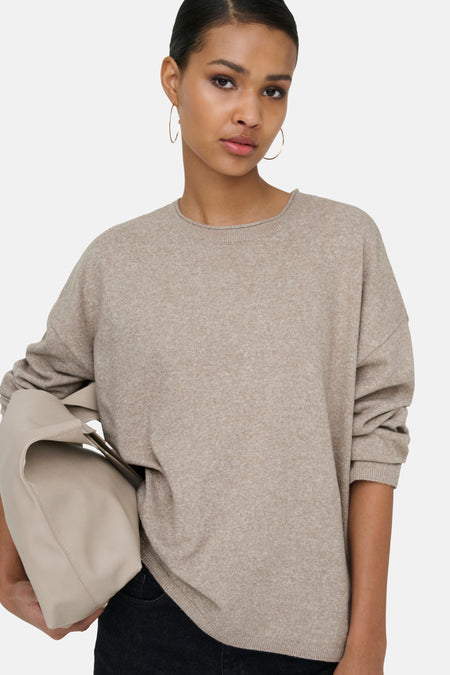 Vrouw met beige trui en tas, gouden oorbellen.