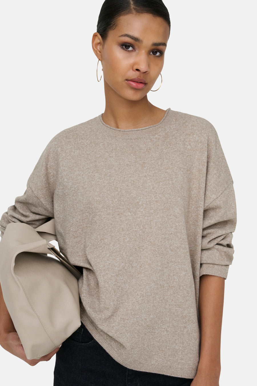Vrouw met beige trui en tas, gouden oorbellen.