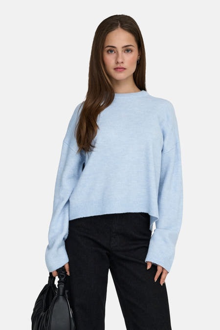 Blauwe trui met ronde hals van ONLY, met lange mouwen en gedragen met een zwarte broek en handtas.