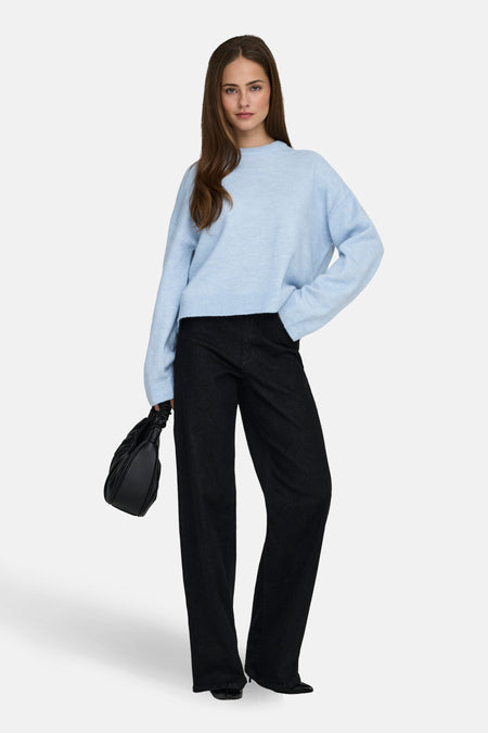 Vrouw in blauwe trui en zwarte broek met tas.