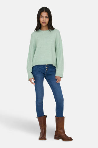 Groene trui met ronde hals van ONLY, gedragen met blauwe jeans met knoopsluiting en bruine leren laarzen.
