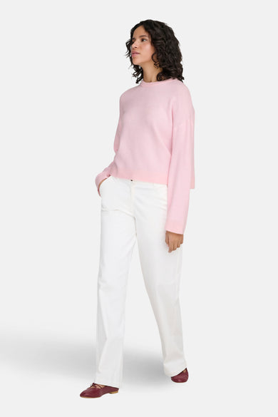Roze trui met ronde hals van ONLY, gedragen met witte broek en bordeauxrode schoenen.
