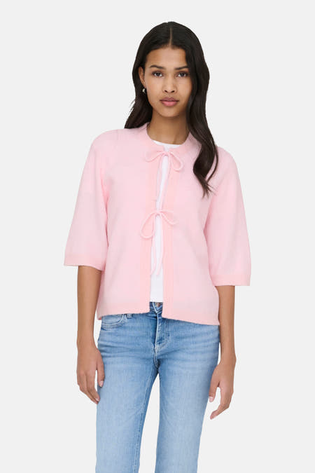 Roze cardigan van ONLY, met korte mouwen en strikdetail, gedragen over een wit shirt en blauwe jeans.
