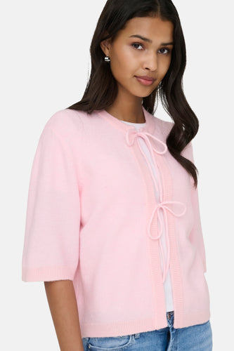 Vrouw in roze vest met strikjes en zilveren oorbellen.