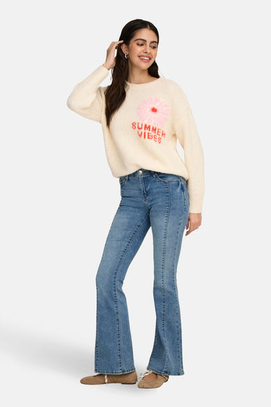 Ecrukleurige trui met ronde hals van ONLY, versierd met een bloemmotief en "Summer Vibes" tekst, gecombineerd met jeans.
