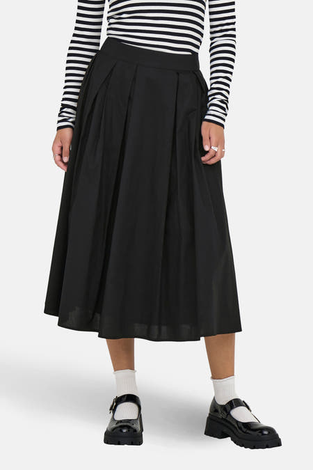 Lange zwarte rok van ONLY, met plooien en een midi-lengte, gedragen met een gestreepte top en zwarte schoenen.
