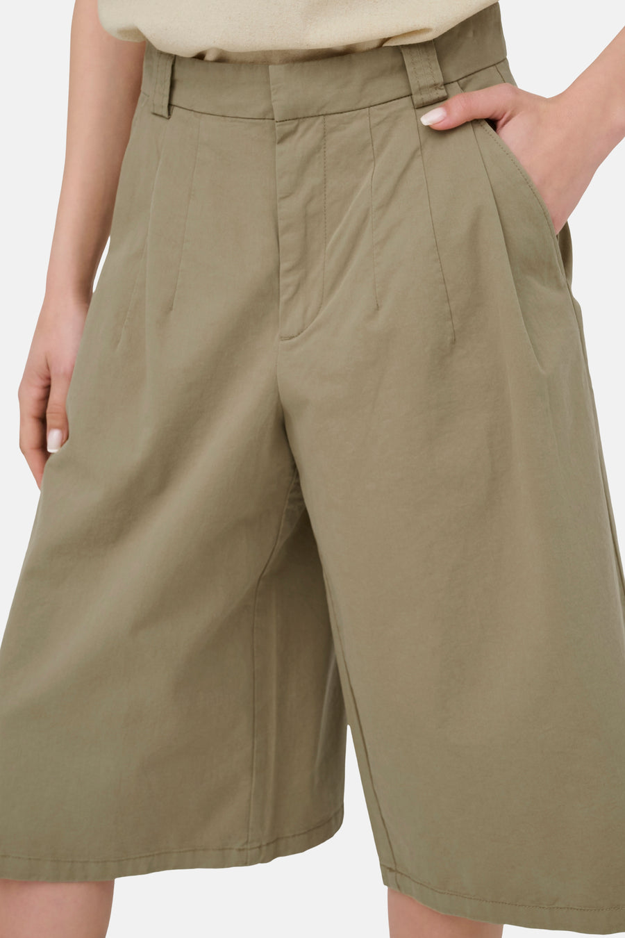 Short vert de JDY à taille haute, avec plis et poches latérales, avec une main dans une poche.