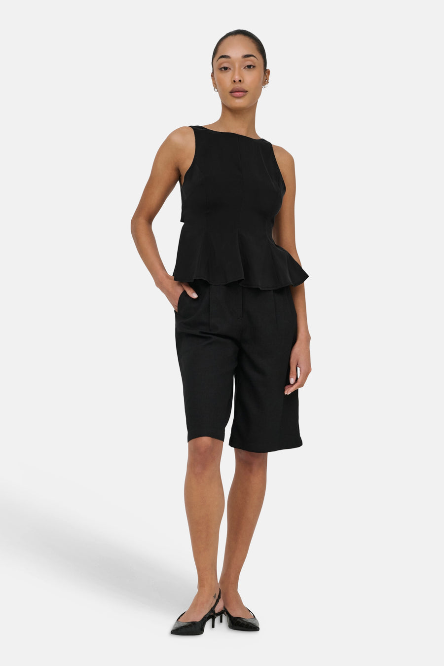 Haut noir sans manches de ONLY avec style péplum, porté avec un short noir et des escarpins slingback.
