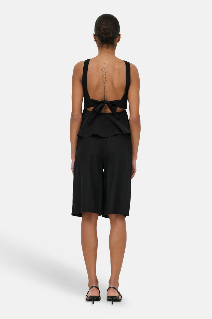 Haut noir sans manches ONLY® avec détail de nœud au dos et ourlet péplum, porté avec un short noir.