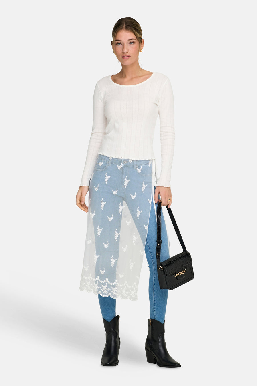Jupe blanche ONLY, avec détails en dentelle, portée sur un jean bleu à broderies florales et des bottes noires.