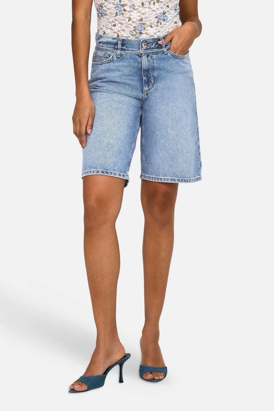 Short en jean bleu mi-long de ONLY®, longueur genou, combiné avec un haut en dentelle blanche et des sandales bleues.
