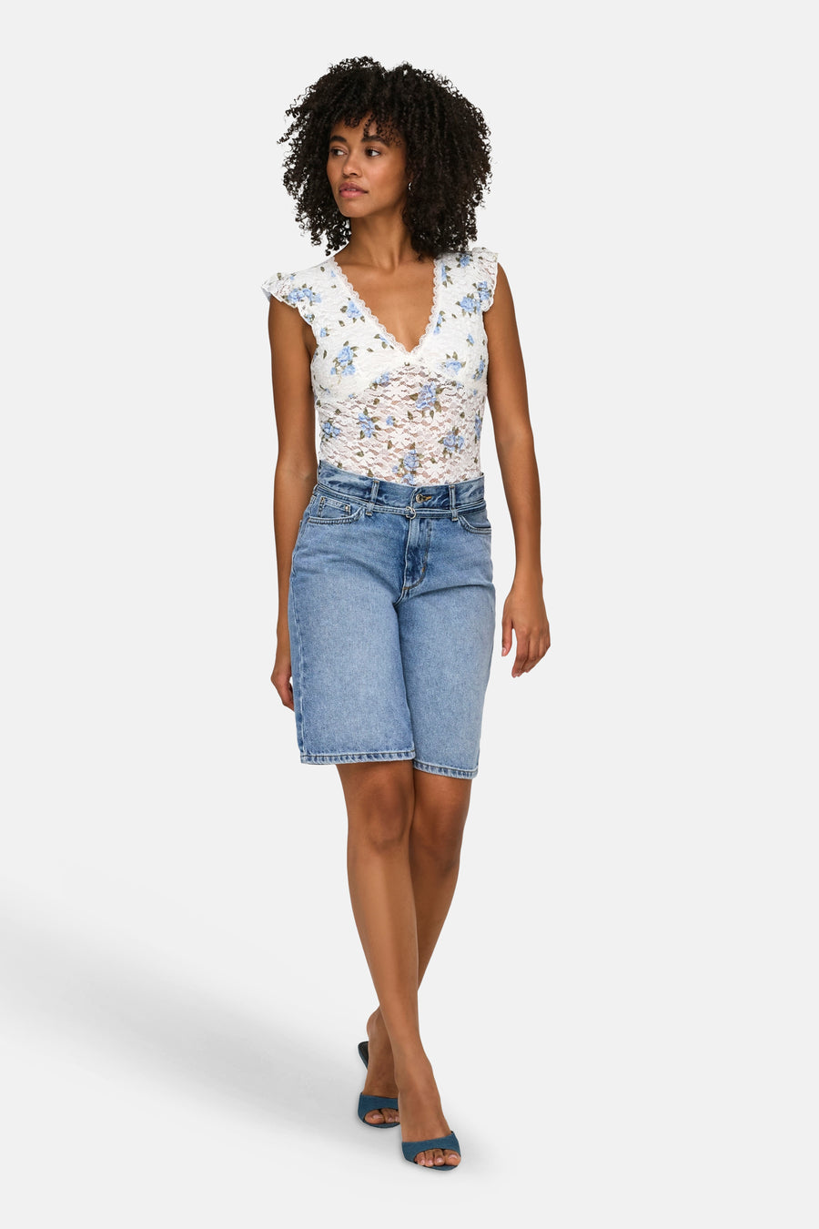 Mid-blauwe denim short van ONLY®, knielengte, gecombineerd met een witte kanten top en blauwe sandalen.