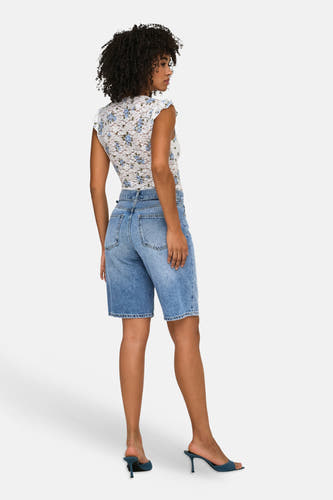 Short en jean bleu moyen de ONLY®, partiellement vue de dos sur un mannequin, combinée avec un haut fleuri en dentelle blanche et des mules bleues.