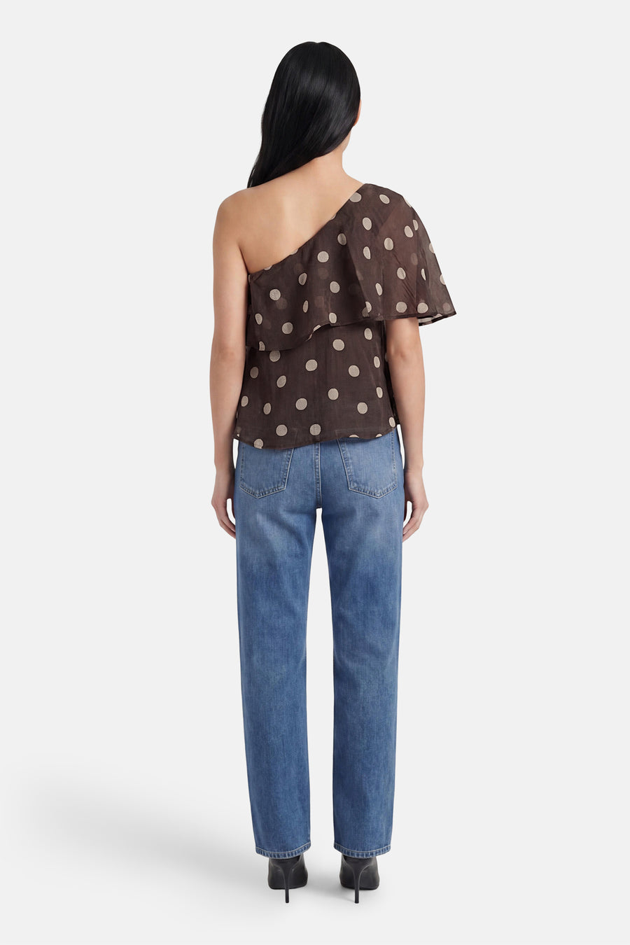 Bruine blouse met korte mouwen van JDY, met witte stippen, één schouder en een ruche, gedragen op de rug met jeans en hakken.