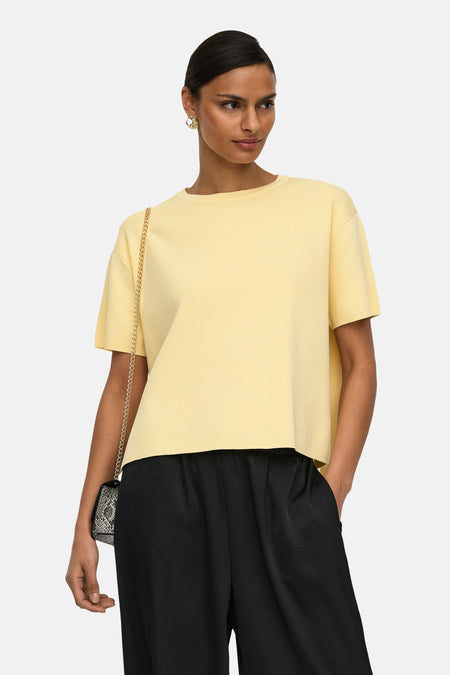 Gele trui met ronde hals van JDY, gedragen met zwarte pantalon en kleine handtas met ketting.
