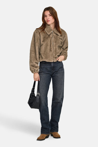 Vrouw draagt bruine jas, donkere jeans, bruine laarzen en zwarte tas.