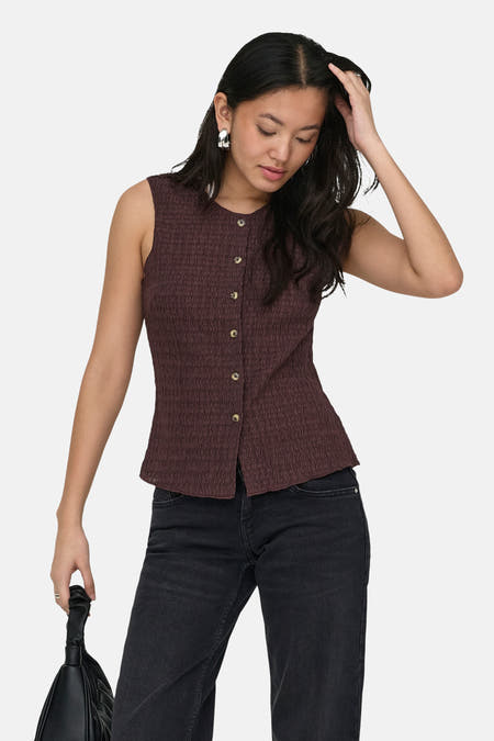 Bruin gilet van ONLY® met knoopsluiting, getextureerde stof en gedragen met zwarte jeans en een handtas.
