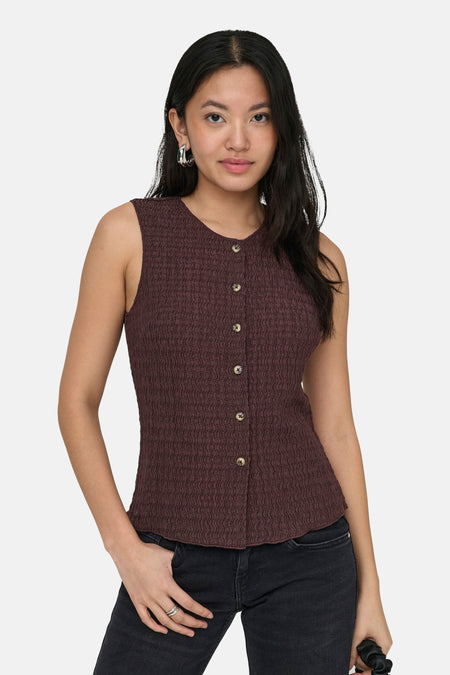 Bruin gilet van ONLY®, met knoopsluiting en een gestructureerde textuur, gecombineerd met zwarte jeans en zilveren oorbellen.
