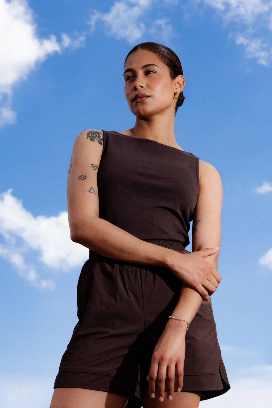 Bruine mouwloze top van ONLY® met asymmetrische halslijn, gedragen met bijpassende korte broek, lifestyle shot tegen blauwe lucht