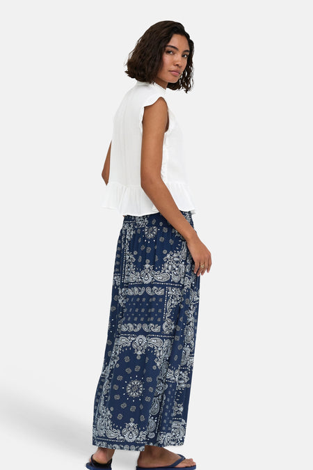 Witte mouwloze blouse met ruches aan de zijkant en zoom, van ONLY®, gedragen met een donkerblauwe paisleyrok, zijaanzicht.