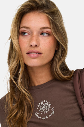 Bruine korte mouwen t-shirt van ONLY® met witte zonprint en tekst, gedragen door model met lang haar, close-up voorzijde