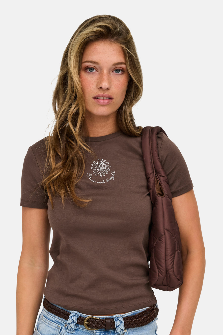 Bruine korte mouwen t-shirt met witte zonprint en tekst, van ONLY®, gedragen met blauwe jeans en gevlochten riem, lifestyle shot